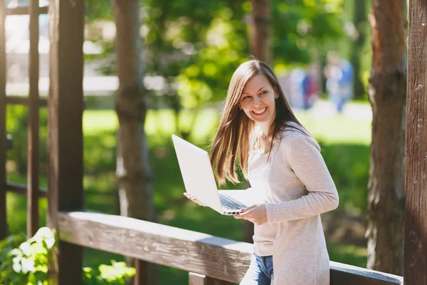 Genç başarılı işkadını hafif rahat kıyafetler içinde. Gülümseyen kadın modern dizüstü pc bilgisayar Şehir Park açık havada bahar doğa üzerinde sokakta üzerinde çalışıyor. Mobil ofis. Serbest iş kavramı