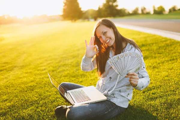 Kadın holding bohça-in dolar nakit para. Dizüstü pc bilgisayar Şehir Park açık havada Güneş çim yeşil çim üzerinde çalıştığı yer, çimenlerin üzerinde oturan bir bayan. Mobil ofis. Serbest iş kavramı