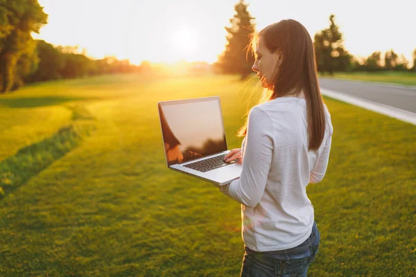 Genç kadın arkadan görünüm. Şehir Parkı yeşil çim Güneş'ın bahçesinde açık havada, uzay kopyalamak için dizüstü pc bilgisayar boş siyah Boþ ekran ile üzerinde çalışan kadın. Mobil ofis. Serbest iş kavramı