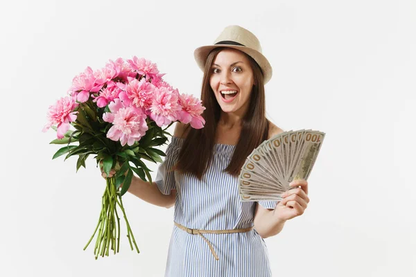 Genç kadın mavi elbiseli, dolar, nakit para, güzel pembe peonies buket demet tutan şapka beyaz arka plan üzerinde izole oldukça mutlu. İş, teslimat, online alışveriş kavramı