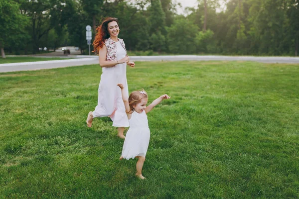 Yetişmeye çalışan ışık içinde neşeli kadın küçük şirin çocuk bebek kız parkta yeşil çimenlerin üzerinde eğlenceli sahip. Anne, küçük çocuk kızı. Anneler günü, aşk aile, ebeveynlik, çocukluk kavramı