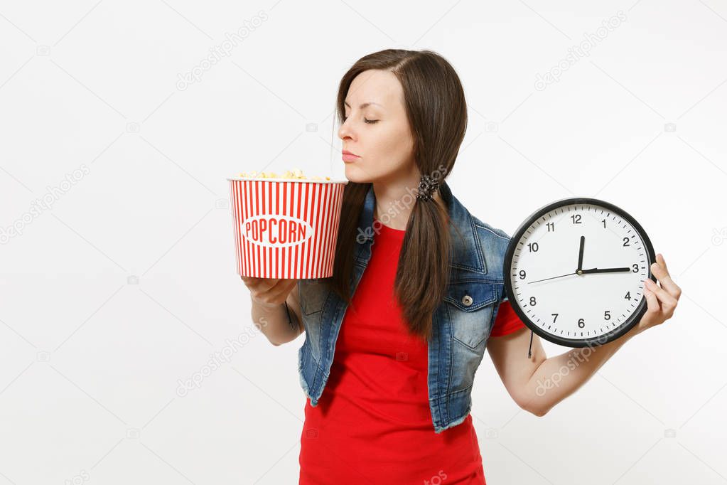 Portrait of young relaxed beautiful brunette woman in casual clothes watching movie film, holding bucket of popcorn and alarm clock, screaming isolated on white background. Emotions in cinema concept