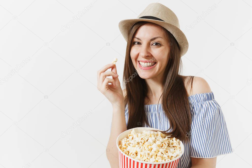 Young woman in blue dress, hat watching movie film holding eating popcorn from bucket isolated on white background. People, sincere emotions in cinema, lifestyle concept. Advertising area. Copy space