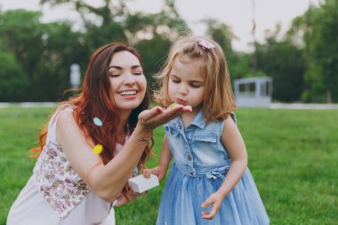 Işık elbise ve küçük şirin çocuk bebek kız oyun renkli kağıt konfeti yeşil park üzerinde üfleme kadında. Anne, küçük çocuk kızı. Anneler günü, aşk aile, ebeveynlik, çocukluk kavramı