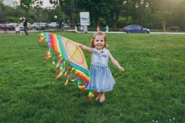 Gülümseyen küçük şirin çocuk bebek kız kot elbise yürüme, renkli uçurtma ile oynamak ve eğlenmek içinde yeşil park. Anne, küçük çocuk kızı. Anneler günü, aşk aile, ebeveynlik, çocukluk kavramı
