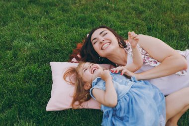 Işık elbise ve küçük şirin çocuk bebek kız çok memnun kadın park dinlenme oyun yeşil çim üzerinde yalan ve eğlenin. Anne, küçük çocuk kızı. Anneler günü, aşk aile, ebeveynlik, çocukluk kavramı