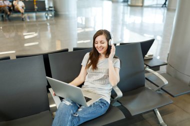 Dizüstü bilgisayar, çalışma müzik dinlerken kulaklık ile seyahat etmek turist gülümseyen genç Uluslararası Havaalanı'nda lobi salonunda bekleyin. Yurt dışında hafta sonu kaçış üzerinde seyahat yolcu. Hava uçuş kavramı