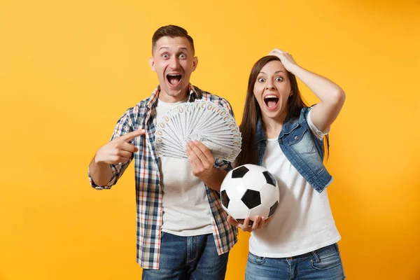 Genç kazanmak çift, kadın erkek, dolar, nakit para, futbol topu, paket tutan futbol taraftarları destek ekibi üzerinde sarı arka plan izole neşelen. Spor bahis heyecan şevk aile yaşam tarzı kavramı