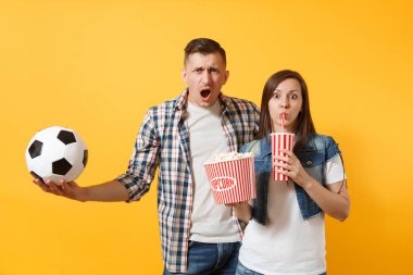 Genç eğlenceli çift, kadın erkek, holding futbol topu, kova patlamış mısır, plastik bardak kola, futbol taraftarları destek ekibi, sarı zemin üzerine izole neşelen. Spor aile eğlence yaşam tarzı kavramı