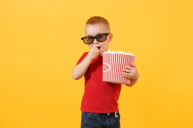 Küçük sevimli oğlu kırmızı t-shirt, patlamış mısır, kova tutarak 3d IMAX sinema gözlük hızlı yemek yeme 3-4 yaşında sarı arka plan üzerinde izole. Çocuklar çocukluk yaşam tarzı kavramı. Kopya alanı