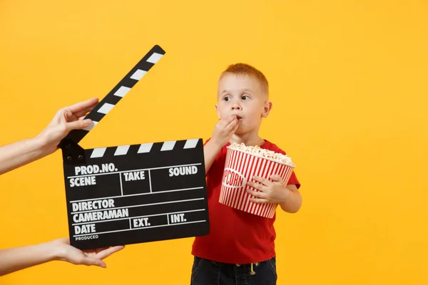 孩子小男孩穿着红色 拿着一桶爆米花 吃着黄色背景下的快餐食品 童年的生活方式概念 不健康的快餐 手部黑膜制作 Clapperboard 复制空间 — 图库照片