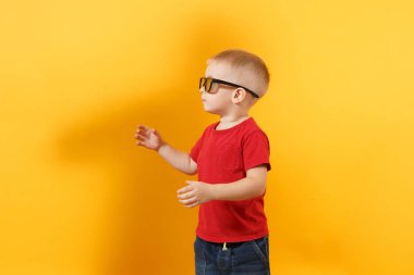 Küçük şirin çocuk bebek çocuk 3-4 yıl içinde kırmızı t-shirt, eski bir kenara plastik cam izole sarı zemin üzerine soda ile el seyir 3d IMAX sinema gözlük. Çocuklar çocukluk yaşam tarzı kavramı. Kopya alanı