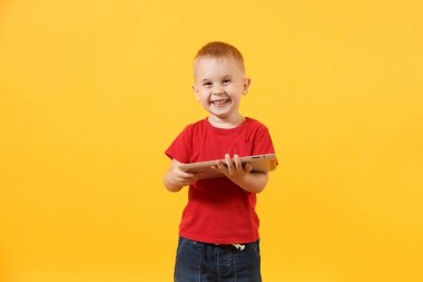 Küçük şirin çocuk bebek çocuk 3-4 yıl içinde elinde tutan tablet pc bilgisayar üzerinde sarı arka plan izole kırmızı t-shirt eski. Çocuklar çocukluk yaşam tarzı kavramı. Sorun çocuk ve becerikli alet. Kopya alanı