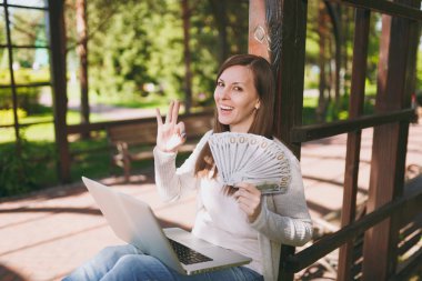 Dolar, nakit para demet tutan genç başarılı işkadını. Şehir Park açık havada doğa üzerinde sokakta modern dizüstü pc bilgisayar üzerinde çalışan kadın. Mobil ofis. Serbest iş kavramı