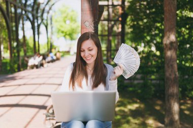 Dolar, nakit para demet tutan genç başarılı işkadını. Şehir Park açık havada doğa üzerinde sokakta modern dizüstü pc bilgisayar üzerinde çalışan kadın. Mobil ofis. Serbest iş kavramı