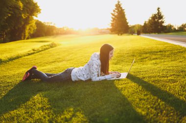 Genç öğrenci rahat kıyafetler içinde kadın akıllı. Çim, dizüstü pc bilgisayar Şehir Park açık havada Güneş çim yeşil çim üzerinde üzerinde çalışıyor yatan kadın. Mobil ofis. Serbest iş kavramı