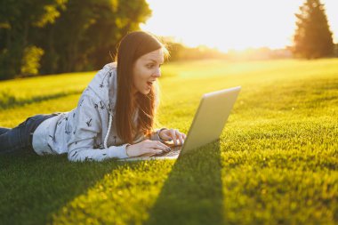 Genç öğrenci rahat kıyafetler içinde kadın akıllı. Çim, dizüstü pc bilgisayar Şehir Park açık havada Güneş çim yeşil çim üzerinde üzerinde çalışıyor yatan kadın. Mobil ofis. Serbest iş kavramı