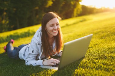 Genç öğrenci rahat kıyafetler içinde kadın akıllı. Çim, dizüstü pc bilgisayar Şehir Park açık havada Güneş çim yeşil çim üzerinde üzerinde çalışıyor yatan kadın. Mobil ofis. Serbest iş kavramı