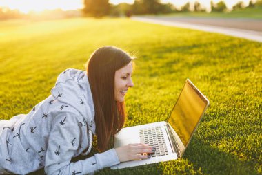 Genç öğrenci rahat kıyafetler içinde kadın akıllı. Çim, dizüstü pc bilgisayar Şehir Park açık havada Güneş çim yeşil çim üzerinde üzerinde çalışıyor yatan kadın. Mobil ofis. Serbest iş kavramı