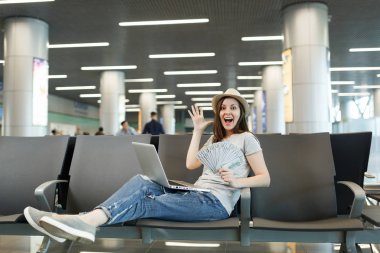 Dizüstü bilgisayarda çalışan sürpriz seyahat etmek turist kadın havaalanında lobi salonunda ellerini dur yayılan dolar nakit para, demet tutun. Hafta sonu kaçamağı yurt dışında seyahat yolcu. Hava uçuş kavramı