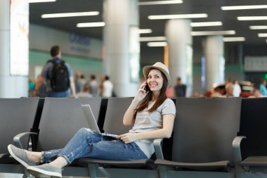 Genç gülümseyen seyahat etmek turist kadın dizüstü bilgisayar, çalışma üstünde hareket eden telefon, çağrı arkadaş, havaalanında lobi salonunda taksi otel bekle rezervasyon konuş. Yurt dışında hafta sonları seyahat yolcu. Hava uçuş kavramı