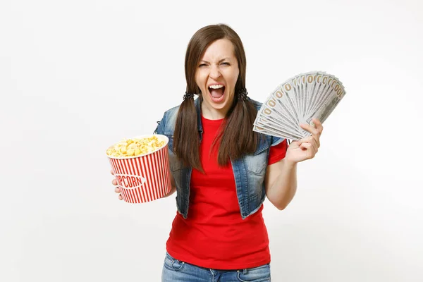 Portrait of young crazy woman in casual clothes watching movie film, holding bucket of popcorn and bundle of dollars, cash money, screaming isolated on white background. Emotions in cinema concept