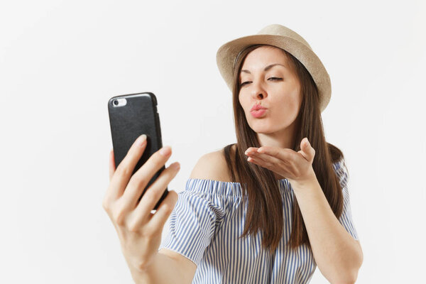 Young woman in blue dress, hat blowing kisses, doing selfie shot on mobile phone or video call isolated on white background. People, sincere emotions, lifestyle concept. Advertising area. Copy space