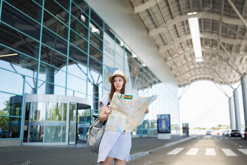 Young traveler tourist woman with backpack standing at international airport, holding paper map. Female passenger traveling abroad to travel on weekends getaway. Air travel, flight journey concept