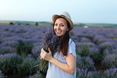 Mavi elbiseli, mor lavanta çiçek çiçek çayır alan açık havada yaz doğa arka plan üzerinde şapka genç şehvetli güzel kadın. İhale kadın kokulu çiçekli çalı yakın. Yaşam tarzı kavramı.