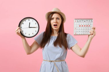 Yuvarlak saat, pembe eğilimleri arka plan üzerinde izole adet gün kontrol etmek için dönemleri takvim tutan mavi elbiseli şok karışık üzgün kadın. Tıbbi jinekolojik kavramı. Kopya alanı