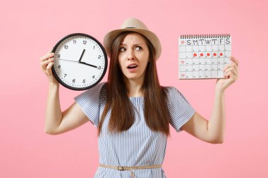 Yuvarlak saat, pembe eğilimleri arka plan üzerinde izole adet gün kontrol etmek için dönemleri takvim tutan mavi elbiseli şok karışık üzgün kadın. Tıbbi jinekolojik kavramı. Kopya alanı