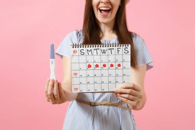 Mutlu kadın mavi elbiseli kırpılmış, şapka tutun el gebelik testi, pembe arka plan izole adet gün kontrol etmek için dönemleri takvim. Tıp, sağlık, jinekolojik kavramı. Kopya alanı
