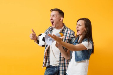 Mutlu genç çift destekçisi, kadın erkek, futbol taraftarları destek ekibi, tezahürat megafon, sarı zemin üzerine izole futbol topu tutan. Spor, aile eğlence, insanların yaşam tarzı kavramı