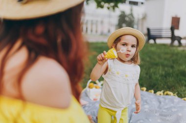 Kadın sarı elbise oyun parkı kalan, çimlerin üzerine sabun köpüğü üfleme ile bebek kız küçük şirin çocuk eğlendirmek. Anne, küçük çocuk kızı. Anneler günü, aşk aile, ebeveynlik, çocukluk kavramı