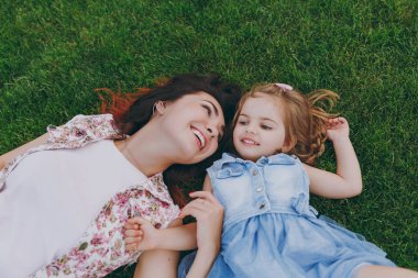 Işık içinde neşeli kadın ve küçük şirin çocuk bebek kız yalan park kalan yeşil çimenlerin üzerinde gülümseyen, iyi eğlenceler. Anne, küçük çocuk kızı. Anneler günü, aşk aile, ebeveynlik, çocukluk kavramı