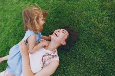 Işık elbise ve küçük şirin çocuk bebek kız çok memnun kadın park dinlenme oyun yeşil çim üzerinde yalan ve eğlenin. Anne, küçük çocuk kızı. Anneler günü, aşk aile, ebeveynlik, çocukluk kavramı