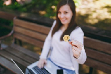 Hafif rahat kıyafetler genç kadın. Bitcoin sikke altın renk modern dizüstü pc bilgisayar açık havada sokakta üzerinde tutarak bankta oturan kadın. Mobil ofis sanal para kavramı