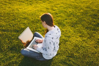 Genç öğrenci kadın rahat kıyafetler. Dizüstü pc bilgisayar Şehir Park açık havada Güneş çim yeşil çim üzerinde çalıştığı yer, çimenlerin üzerinde oturan bir bayan. Mobil ofis. Serbest iş kavramı