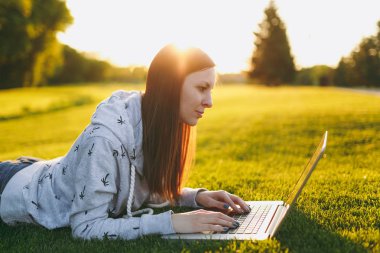 Genç öğrenci rahat kıyafetler içinde kadın akıllı. Çim, dizüstü pc bilgisayar Şehir Park açık havada Güneş çim yeşil çim üzerinde üzerinde çalışıyor yatan kadın. Mobil ofis. Serbest iş kavramı