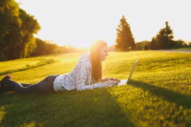 Genç öğrenci rahat kıyafetler içinde kadın akıllı. Çim, dizüstü pc bilgisayar Şehir Park açık havada Güneş çim yeşil çim üzerinde üzerinde çalışıyor yatan kadın. Mobil ofis. Serbest iş kavramı