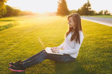 Genç öğrenci kadın rahat kıyafetler. Dizüstü pc bilgisayar Şehir Park açık havada Güneş çim yeşil çim üzerinde çalıştığı yer, çimenlerin üzerinde oturan bir bayan. Mobil ofis. Serbest iş kavramı