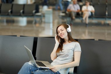 Dizüstü bilgisayarda çalışan müzik dinlerken kulaklık ile seyahat etmek turist kadın genç rahat, Uluslararası Havaalanı'nda lobi salonunda bekleyin. Yurt dışında hafta sonu kaçış üzerinde seyahat yolcu. Hava uçuş kavramı