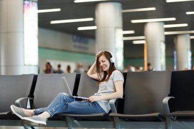 Genç güzel gezgin turist kadın dizüstü bilgisayarda çalışan müzik dinlerken kulaklık ile Uluslararası Havaalanı'nda lobi salonunda bekleyin. Hafta sonu kaçamağı yurt dışında seyahat yolcu. Hava uçuş kavramı