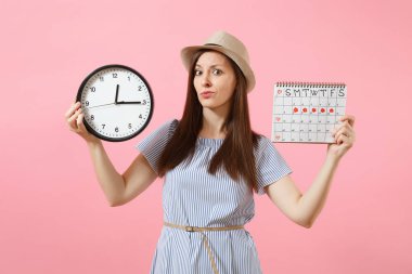 Yuvarlak saat, pembe eğilimleri arka plan üzerinde izole adet gün kontrol etmek için dönemleri takvim tutan mavi elbiseli şok karışık üzgün kadın. Tıbbi jinekolojik kavramı. Kopya alanı