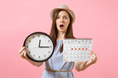 Yuvarlak saat, pembe eğilimleri arka plan üzerinde izole adet gün kontrol etmek için dönemleri takvim tutan mavi elbiseli şok karışık üzgün kadın. Tıbbi jinekolojik kavramı. Kopya alanı