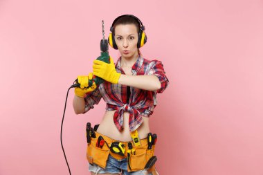 Enerji seksi tamirci kadın eldiven, gürültü yalıtımlı kulaklıklar, Seti Araçları, pembe arka plan izole elektrikli matkap tutan araçların tam kemer. Kadın erkek iş. Yenileme kavramı
