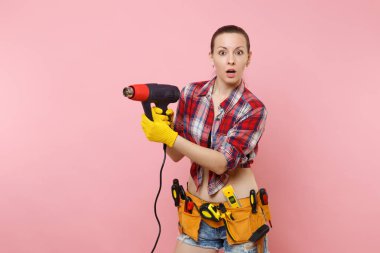 Genç güzel ev erkeği kadın ekose gömlek, kot şort, kit araçları kemer, pembe arka plan izole güç ısı silah tutan çeşitli araçların tam eğlenceli. Kadın erkek iş. Yenileme kavramı
