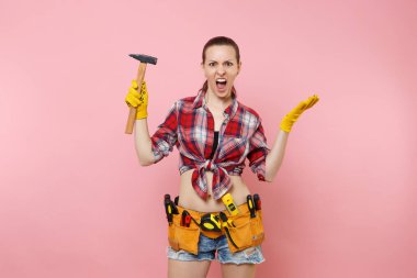 Giyen ekose gömlek, kot şort, kit araçları kemer, pembe arka plan izole farklı enstrümanlar çekiç dolu güçlü genç tamirci kadın. Kadın erkek iş. Yenileme ve işgal kavramı