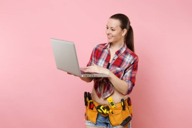 Genç mutlu ev erkeği kadın Kullanıcı ekose gömlek, kot şort, Seti Araçları, pembe arka plan izole dizüstü pc bilgisayar üzerinde çalışan araçların tam kemer. Kadın erkek işi. Yenileme kavramı