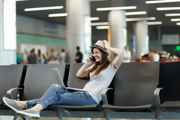 Dizüstü bilgisayarda çalışan seyahat etmek turist kadın gülüyor genç üstünde hareket eden telefon, çağrı arkadaş, havaalanında lobi salonunda taksi otel bekle rezervasyon konuş. Yurt dışında hafta sonları seyahat yolcu. Hava uçuş kavramı